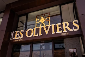 The exterior of the Les Oliviers Hotel with a prominent sign indicating it is a restaurant.