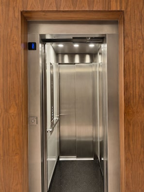 An elevator with a metallic interior, a control panel with a button, and a wooden frame around the door.