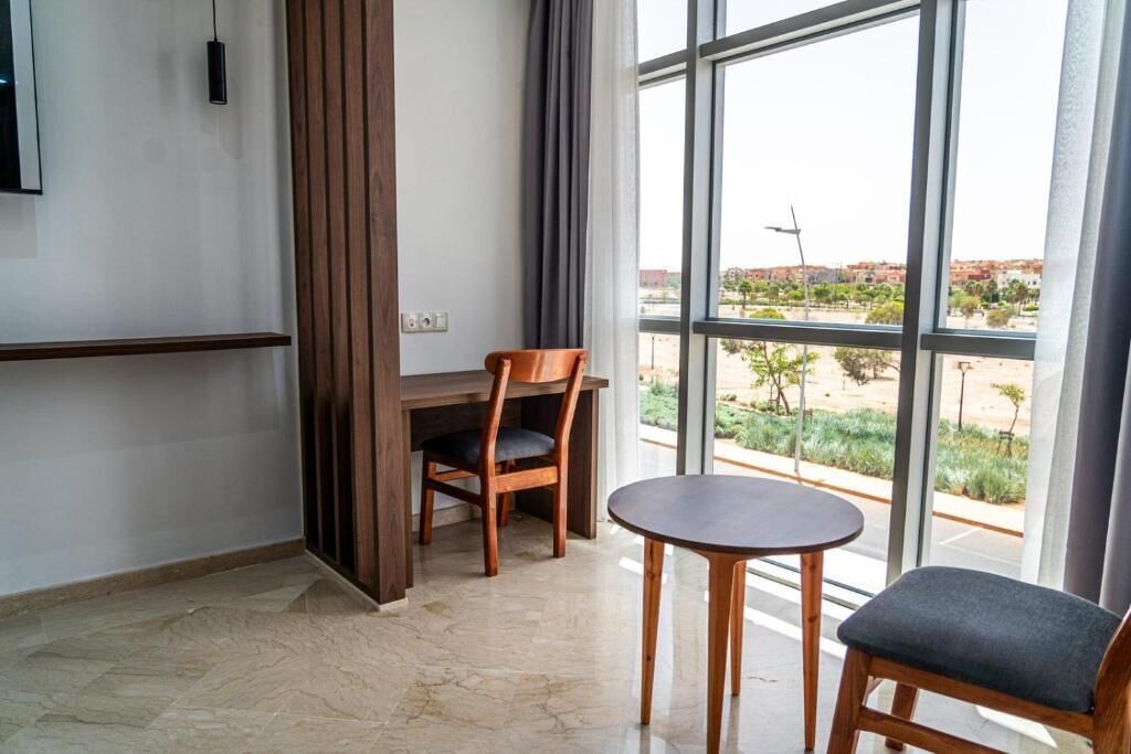 A room with a large window, a wooden desk, a chair, and a small table.