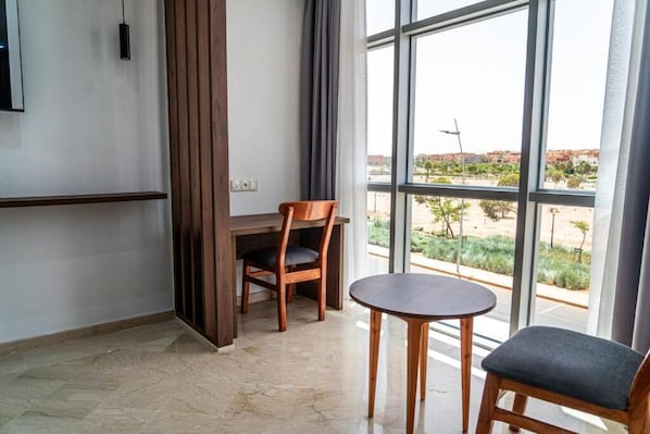 Una habitación con un ventanal grande, un escritorio de madera, una silla y una mesita.