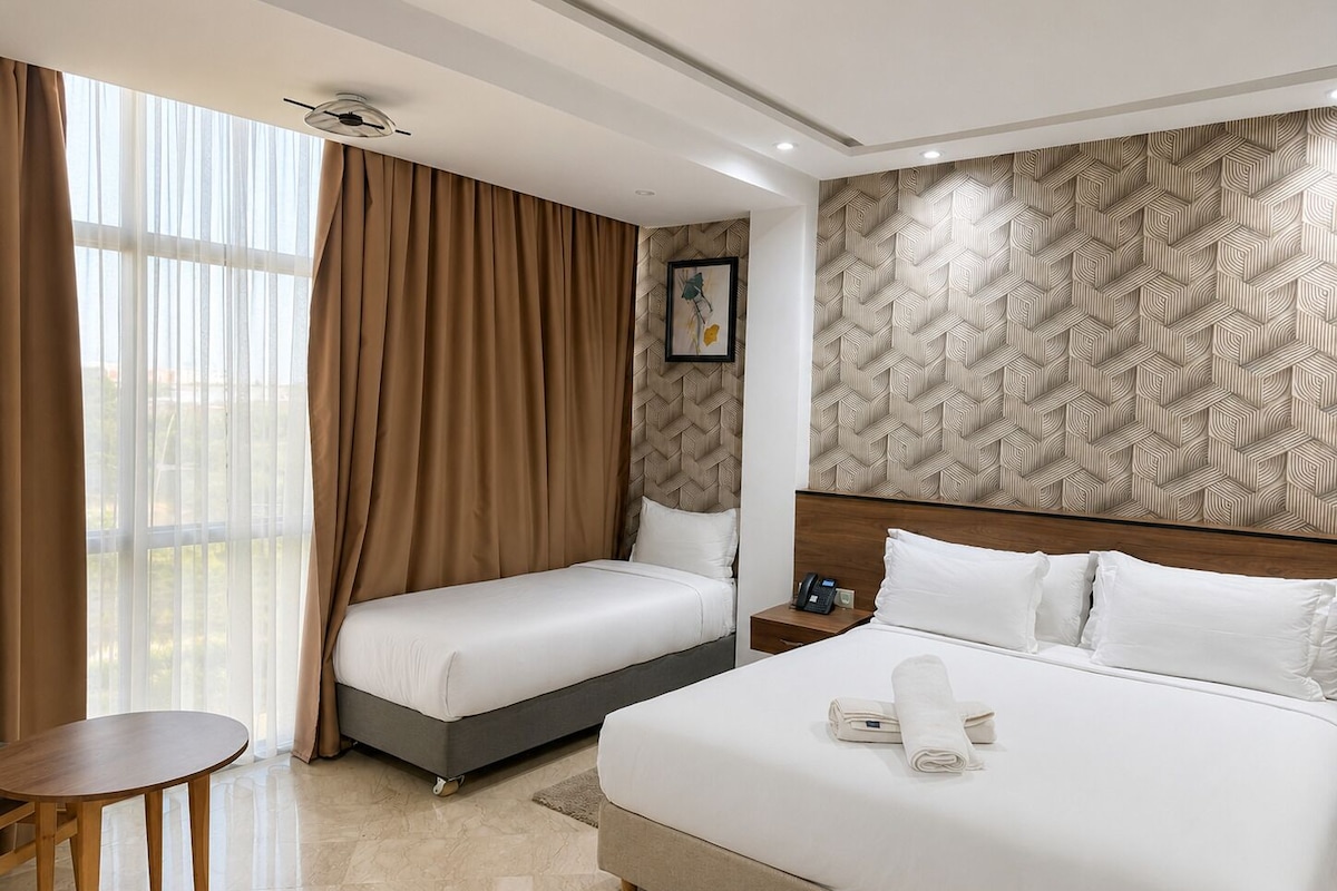 A hotel room with a large bed, a smaller bed, a desk, and a window with curtains.