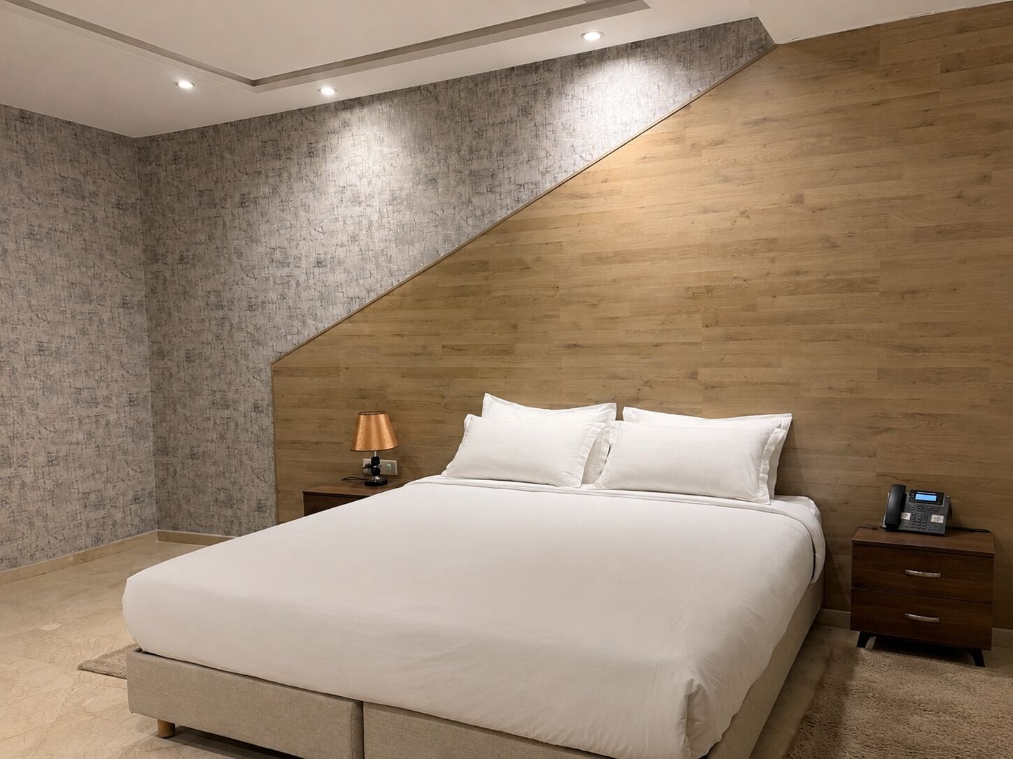 A modern bedroom with a bed, a nightstand, a lamp, and a telephone.