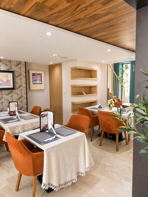 A modern dining area with tables set for two, featuring a wooden ceiling and a view of a staircase.