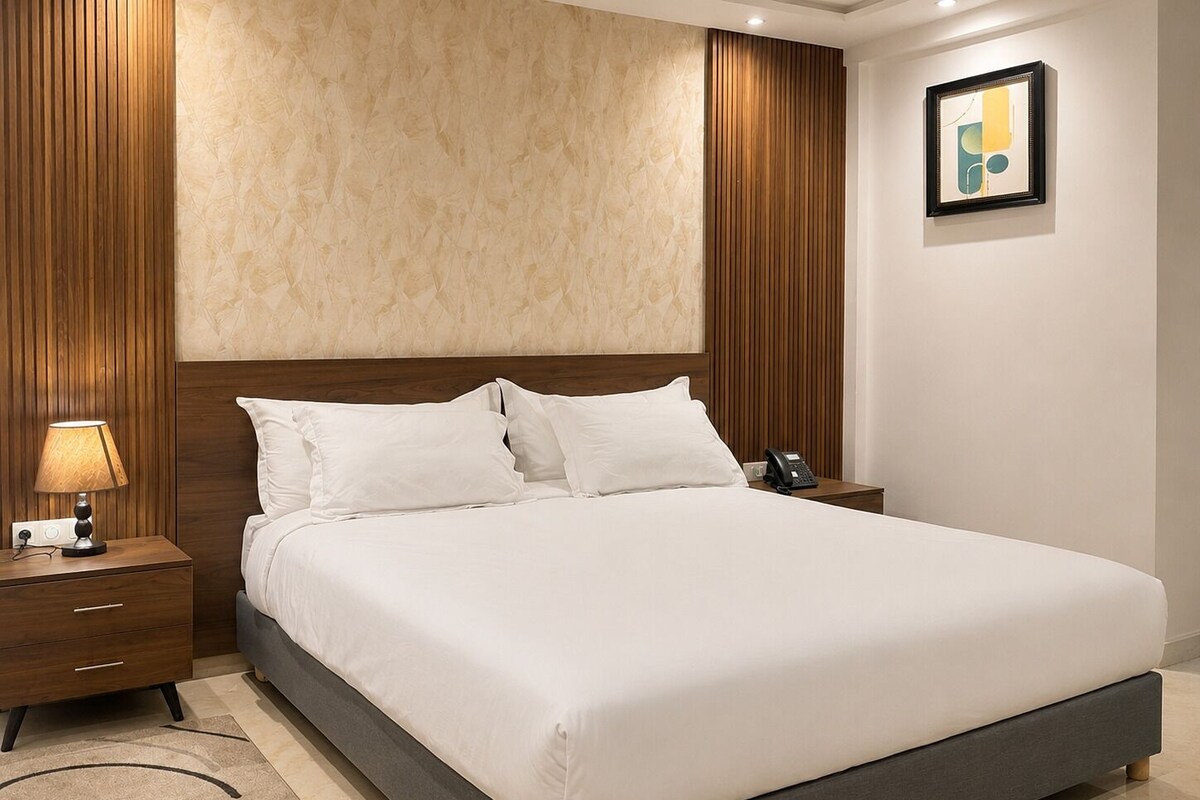 A hotel room with a large bed, a bedside lamp, a phone on the nightstand, and a framed picture on the wall.