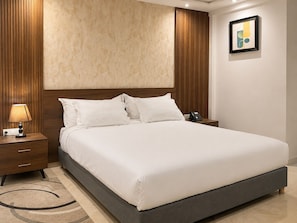 A hotel room with a large bed, a bedside lamp, a phone on the nightstand, and a framed picture on the wall.