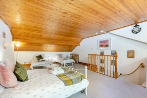 A bedroom with a sloped ceiling, two beds, a small desk, and a staircase with a wooden railing. - 3 Bed in Brixham (oc-c42670) (Brixham)