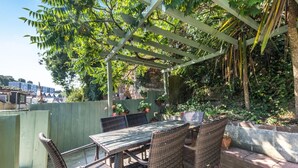 An outdoor patio with a table and chairs, surrounded by greenery and a pergola structure. - 3 Bed in Brixham (oc-c42670) (Brixham)