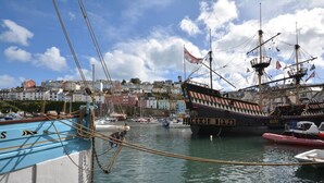 A harbor with a large sailing ship docked, surrounded by smaller boats and buildings in the background. - 3 Bed in Brixham (oc-c42670) (Brixham)