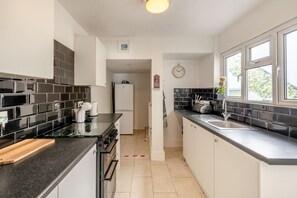 A modern kitchen with black and white tiles, a stainless steel sink, and a built-in oven. - 3 Bed in Brixham (oc-c42670) (Brixham)