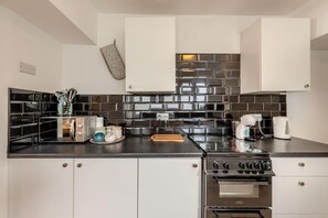 A modern kitchen with black and white tiles, stainless steel appliances, and a built-in oven. - 3 Bed in Brixham (oc-c42670) (Brixham)