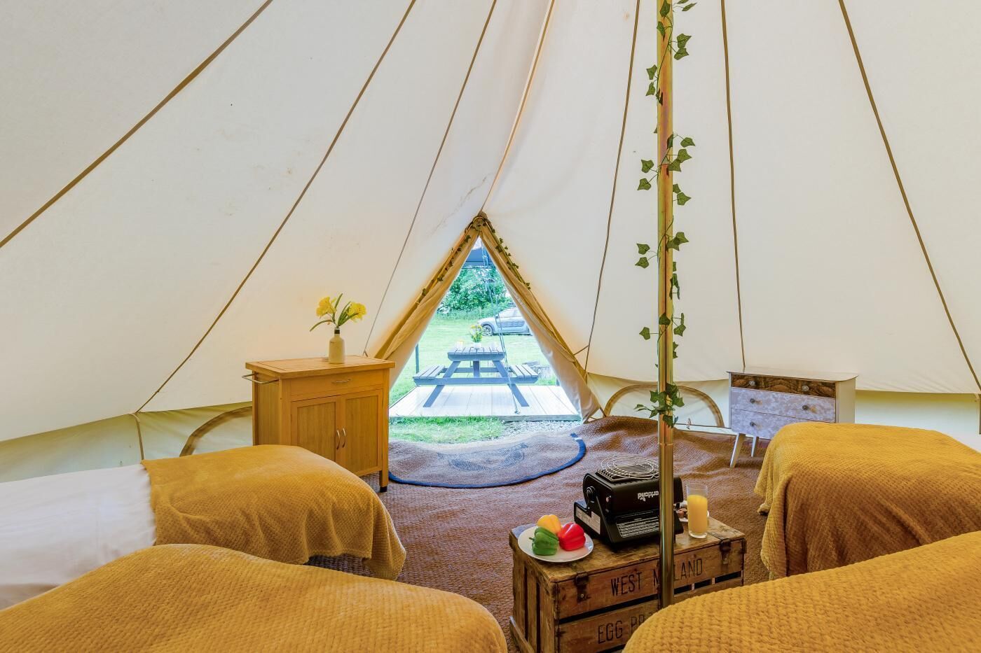 A tent with two beds, a small table, and a view of an outdoor picnic area.
