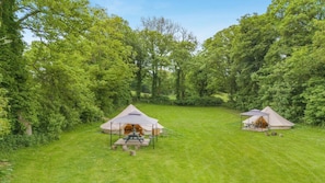 Ein Campingplatz mit zwei Zelten, jeweils mit einem Picknicktisch, umgeben von üppiger Vegetation.