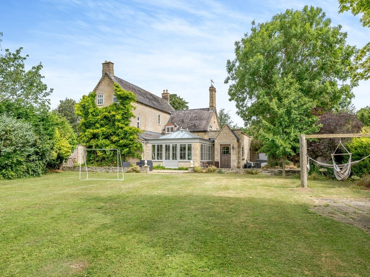 A stone house with a conservatory, a fenced yard, and a hammock.