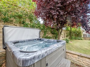A hot tub with a cover, set against a stone wall and surrounded by greenery. - 5 Bed in Burton Pedwardine (oc-g42735) (Burton Pedwardine)