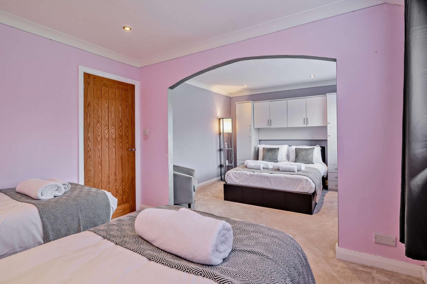 A bedroom with two beds, a wooden door, a wardrobe, and a bathroom visible through an archway.