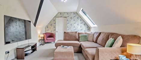 A cozy living room with a large flat-screen TV, a brown sofa, a pink armchair, and a small table with two blue cups.