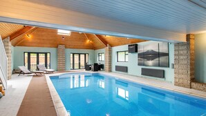 Una piscina interior con piso de baldosas, sillas de descanso y una pared de piedra con un mural.