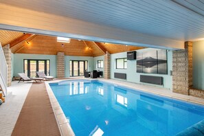 Ein Innenpool mit gefliestem Boden, Liegestühlen und einer Steinwand mit Wandgemälde.