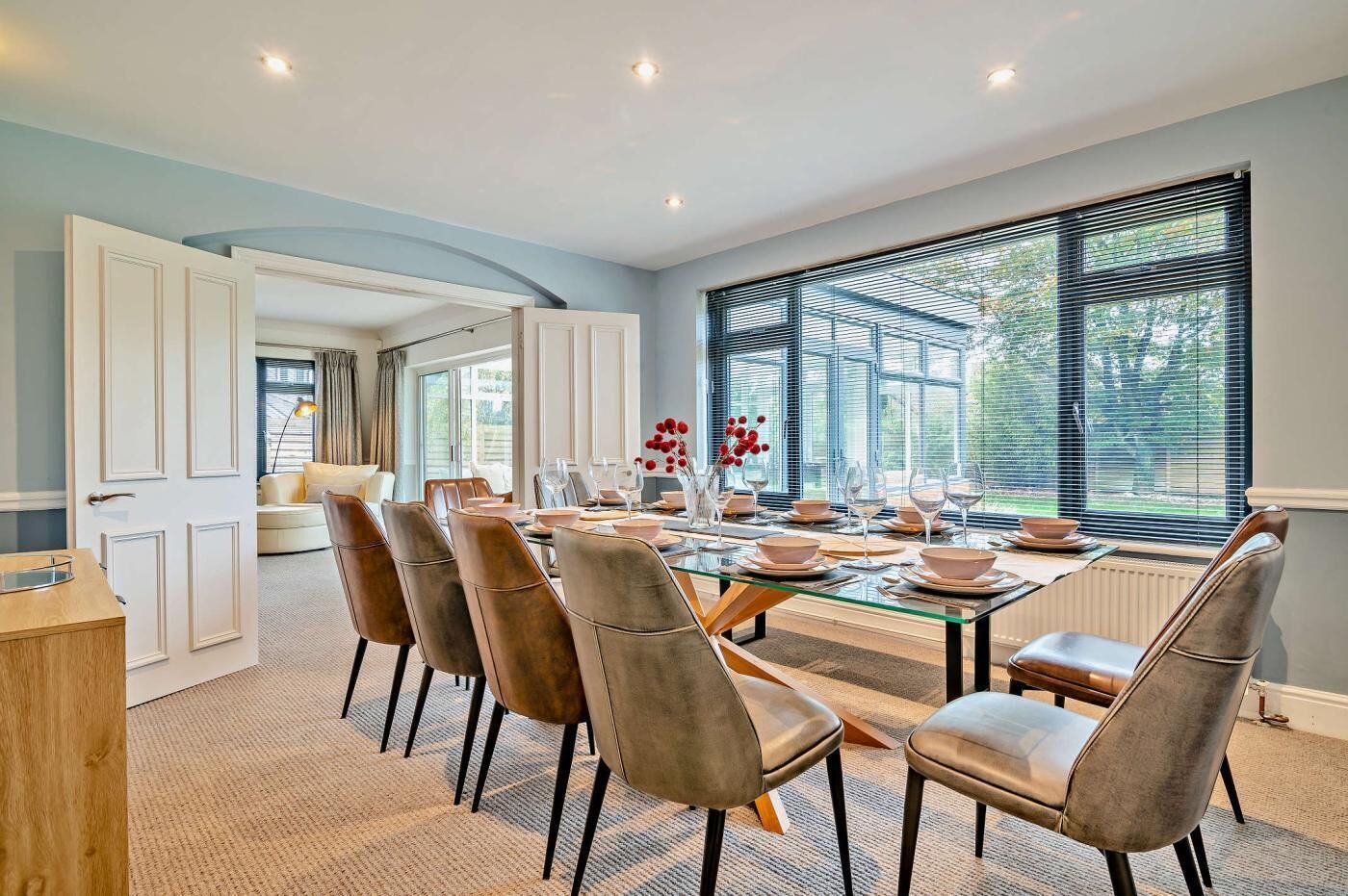 A dining area with a glass table, chairs, and a view of the outdoors through large windows.