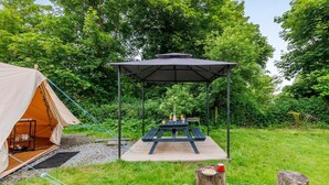En campingopsætning med et telt, et picnicbord og et overdækket siddeområde.