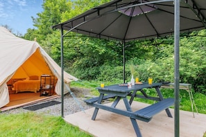 Ein Zelt mit einem Bett und einem Tisch mit Frühstücksgebäck, eingebettet in eine bewaldete Landschaft mit einem Pavillon darüber.