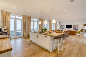 Eine moderne Küche mit einer zentralen Kochinsel, Barhocker und einem Essbereich mit einer Couch und Stühlen.