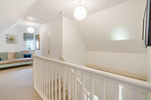 Ein geräumiger Flur mit weißer Treppe, einer Couch mit Karokissen und einer Deckenleuchte.