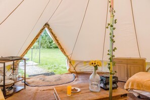 Ein Zeltinnenraum mit Esstisch, Bett, kleiner Kommode und Blick ins Freie.