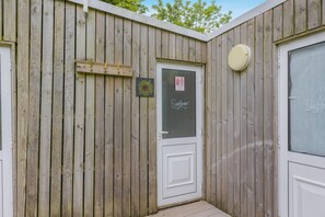 A wooden exterior wall with a white door, a small sign with a sunflower, and a circular object on the right. - 1 Bed in St. Florence (oc-s33553) (Saint Florence)