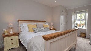 Quarto com cama, mesas de cabeceira, janela e porta.