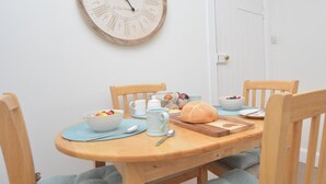 Uma sala de jantar com uma mesa de madeira, cadeiras, um relógio e uma porta ao fundo.