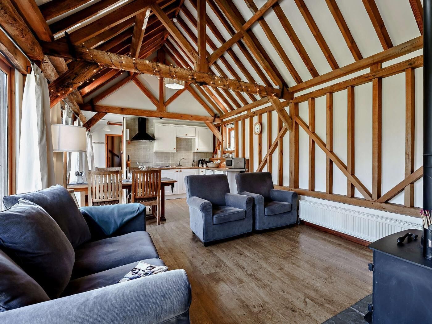 A spacious living area with a high ceiling and exposed wooden beams, a kitchen in the background, and a cozy seating arrangement.