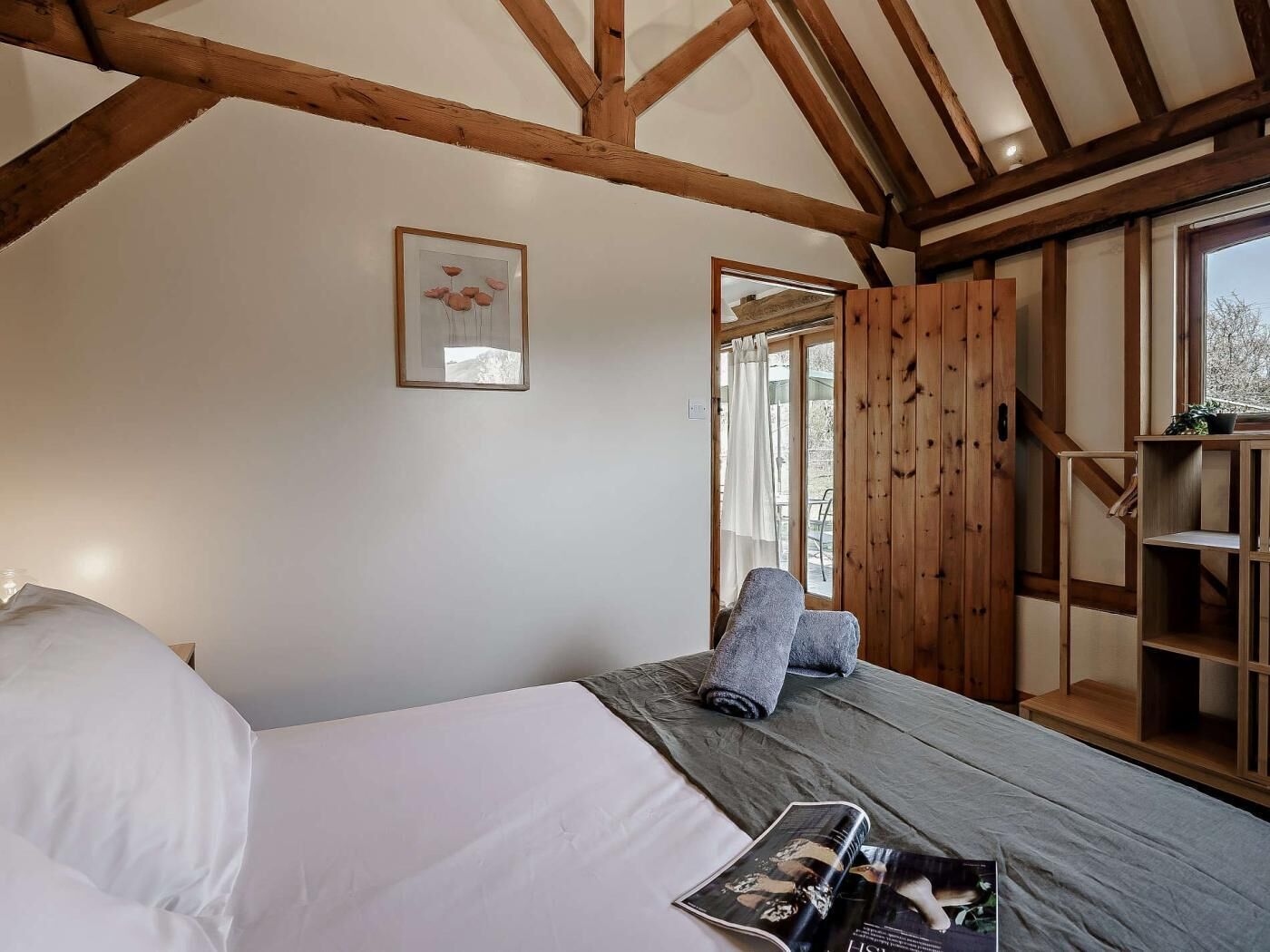 A bedroom with a bed, a window, a wooden bookshelf, and a framed picture on the wall.
