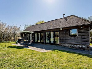 A wooden cabin with a covered patio, large windows, and a chimney. - 2 Bed in Brighton (oc-80378) (Poynings)