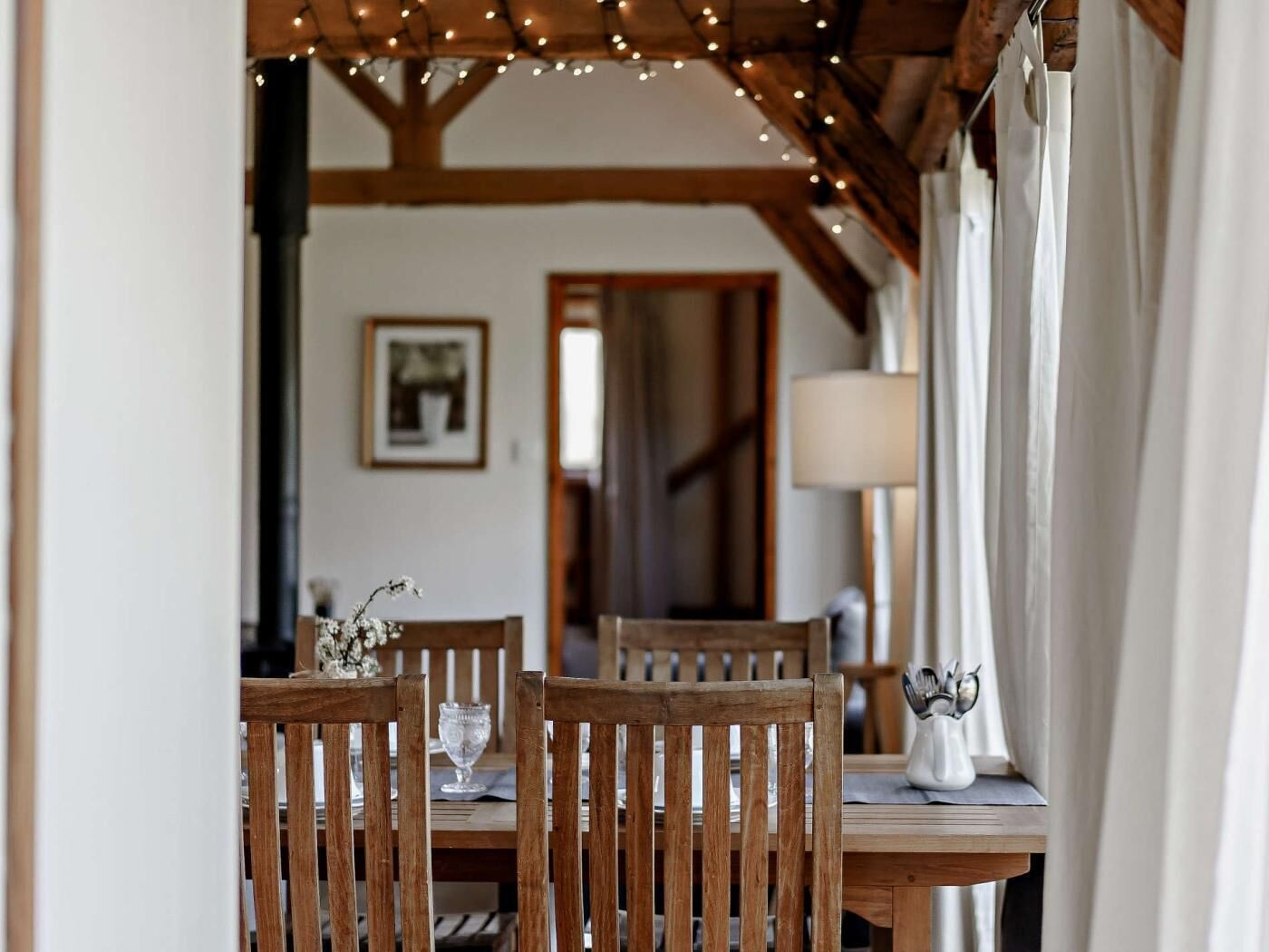 A dining area with wooden chairs and a table, string lights overhead, and a lamp on the table.