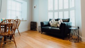 A living room with a black leather sofa, wooden chairs, a small table, and a radiator. - 1 Bed in Tenby (oc-85705) (Tenby)