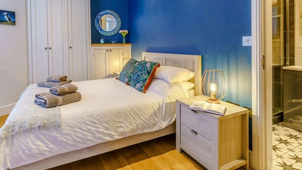 A bedroom with a bed, bedside table, and a mirror. - 1 Bed in Tenby (oc-85705) (Tenby)