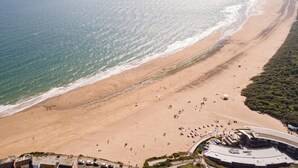 An aerial view of a beach with a curved promenade, a sandy shoreline, and a large building with a flat roof. - 1 Bed in Tenby (oc-85705) (Tenby)