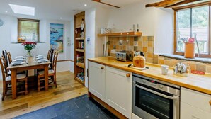 A kitchen with wooden cabinets, a dining table set for four, and a window with a view. - 3 Bed in Launceston (oc-89030) (Egloskerry)
