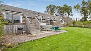 A two-story stone house with a wooden deck, a barbecue grill, and a picnic table. - 2 Bed in Blairgowrie (oc-92113) (Blacklunans)