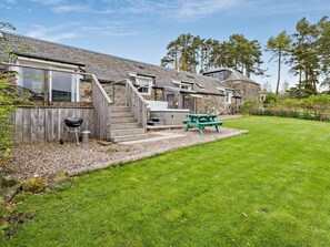 Ein zweistöckiges Steinhaus mit einer Holzterrasse, einem Grill und einem Picknicktisch.