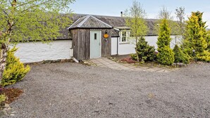 A small wooden shed with a door and a window, surrounded by gravel and greenery. - 2 Bed in Blairgowrie (oc-92113) (Blacklunans)