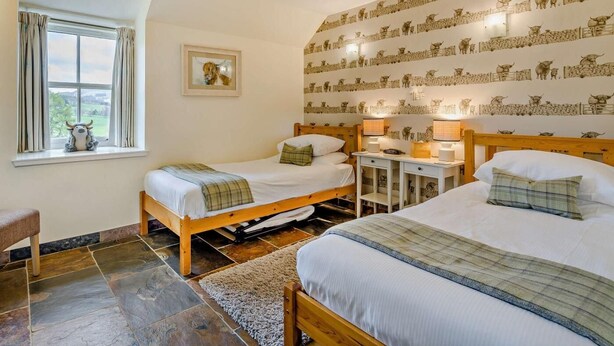 A room with two wooden beds, a small table, a chair, a window with curtains, and a wall with a patterned design. - 2 Bed in Blairgowrie (oc-92113) (Blacklunans)
