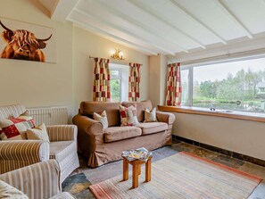 Ein Wohnzimmer mit braunem Sofa, gestreifte Sessel, einem kleinen Holztisch und Seeblick durch ein Fenster.