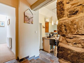 Ein modernes Interieur mit einer Wand aus Stein, einer Küchenzeile mit Esstisch und einem Flur, der in einen weiteren Raum führt.