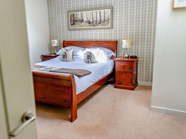 Un letto ben rifatto con struttura in legno, due comodini con lampade, un quadro appeso al muro e un pavimento coperto di moquette.