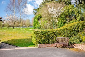 A bench in a landscaped area with a hedge and trees in the background. - 1 Bed in Milton Abbas (oc-a35016) (Milton Abbas)