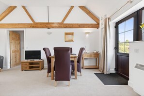 A room with a wooden ceiling, a dining table with chairs, a television, and a door leading outside. - 1 Bed in Milton Abbas (oc-a35016) (Milton Abbas)