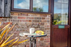 A brick wall with a window, a door, and a small round table with a cup and a plate with food. - 1 Bed in Milton Abbas (oc-a35016) (Milton Abbas)