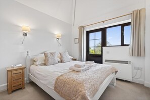 A bedroom with a bed, bedside lamps, a window with curtains, a radiator, and a nightstand with a drawer. - 1 Bed in Milton Abbas (oc-a35016) (Milton Abbas)